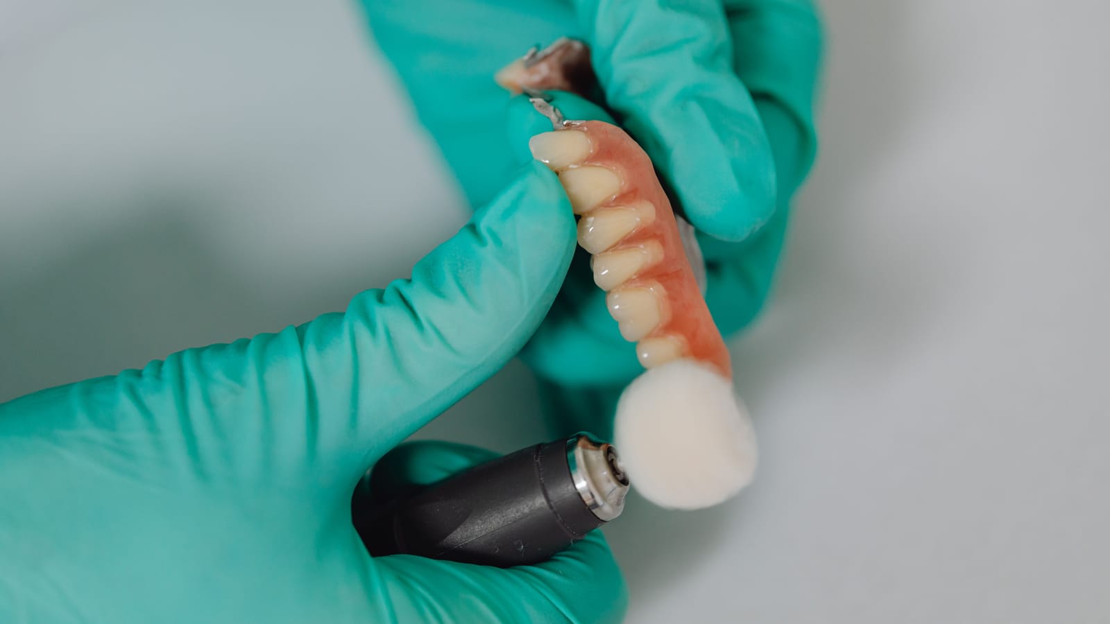 KI in Zahnarztpraxis und Dentallabor prüft Aufträge und erklärt Kostenpläne. Ein Zahntechniker poliert mit behandschuhten Händen eine Prothese am Handstück.