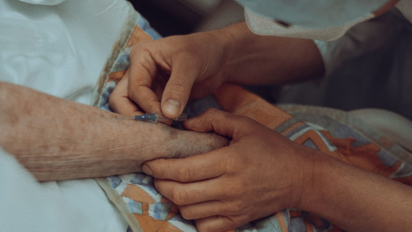 KI in der Pflege übernimmt Dokumentation und Planung, nicht die Arbeit am Menschen. Eine Pflegekraft versorgt die Hand einer älteren Person am Bett.