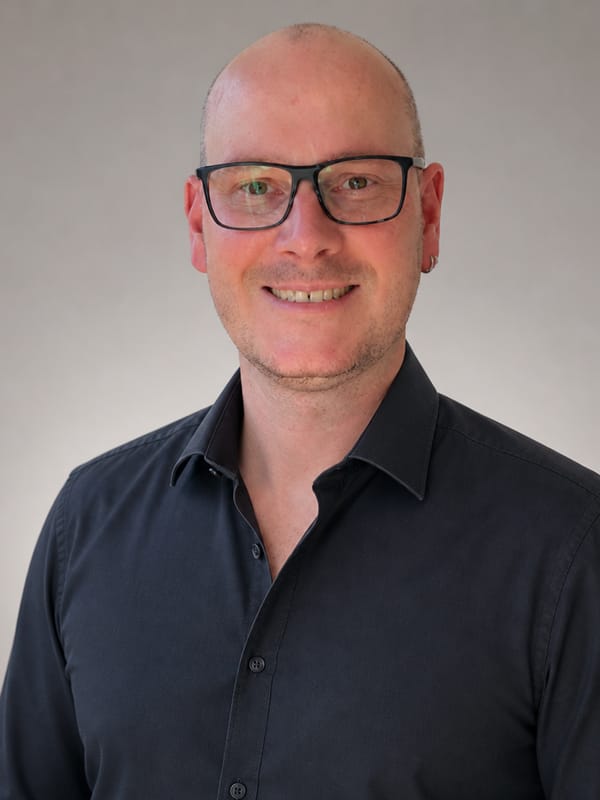 Martin Scholz, Inhaber der KI-Agentur Th&uuml;ringen in Erfurt. Portr&auml;t vor neutralem Hintergrund, dunkles Hemd, Brille. (Hintergrund und Kleidung KI-bearbeitet)
