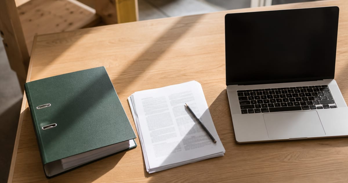 Die KI-Kompetenzpflicht aus Art. 4 verlangt einen nachvollziehbaren Nachweis, keine bestimmte Schulungsform. Aufsicht auf einen geschlossenen Ordner und einen Stapel bedruckter Seiten neben einem Laptop. (KI-generierte Illustration)